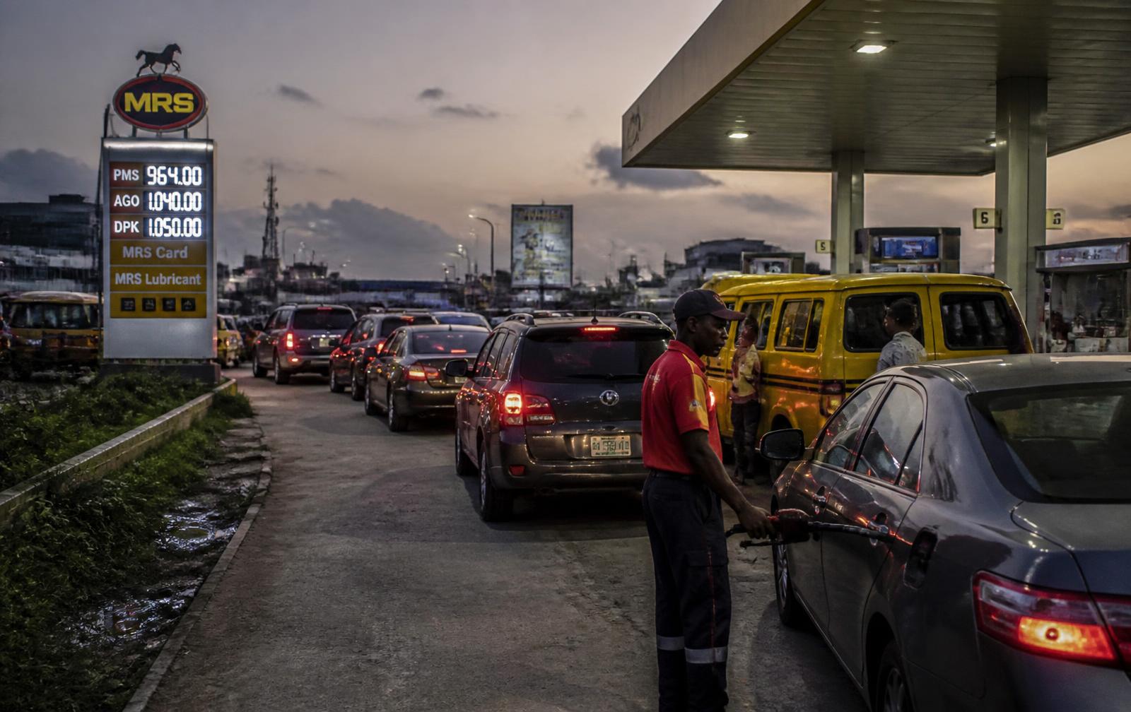 Cars queueing at a Nigerian petrol station at dusk with the pump price board lit